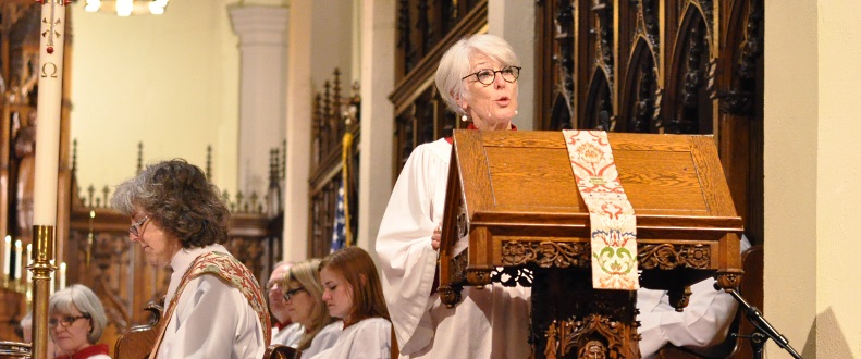 Woman reads at lectern with choir in background