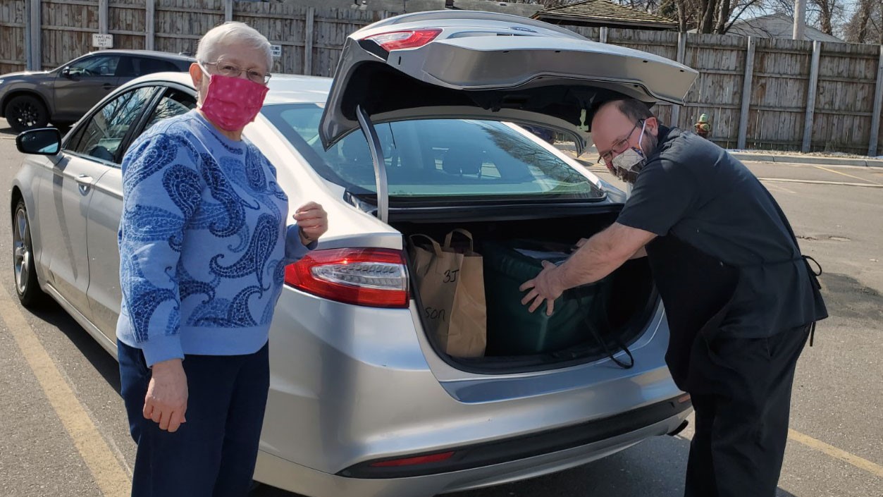 Two people wearing masks loading meals into a car trunk
