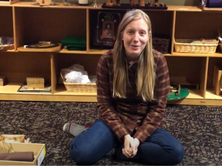 A woman sits on the floor with a box of Montessori objects next to her