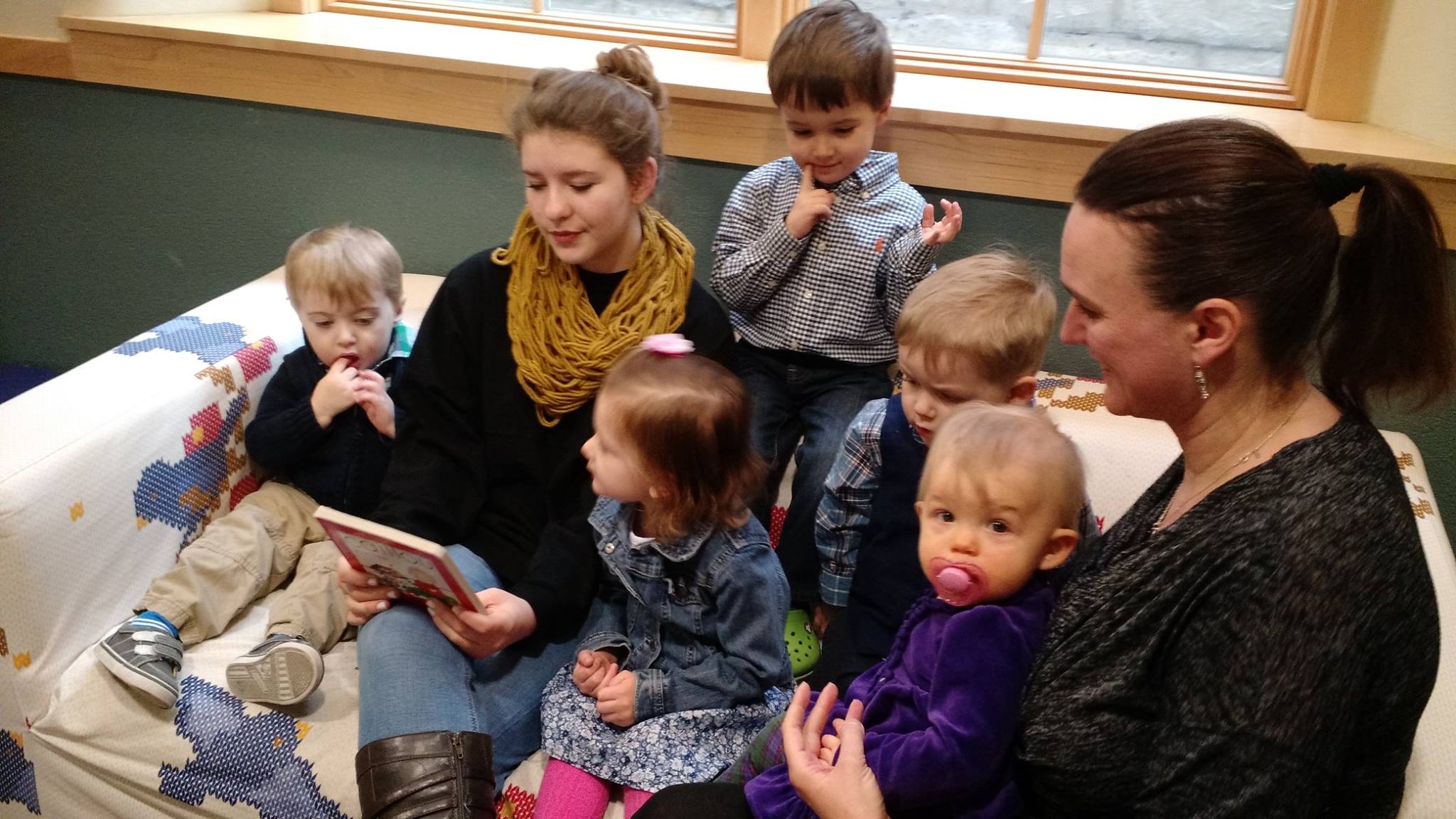 A woman reading a story out loud while sitting on a couch surrounded by kids