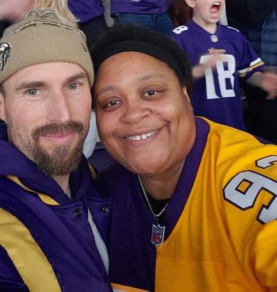 Chris and his wife Angie pose for a selfie in the stands at a football game, both decked head to toe in purple and yellow Vikings gear.