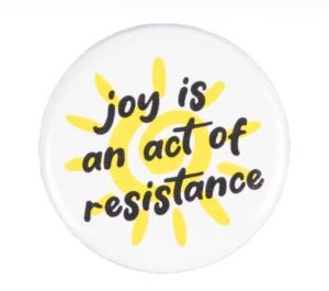 A circular graphic with a yellow sun and the words "joy is an act of resistance"